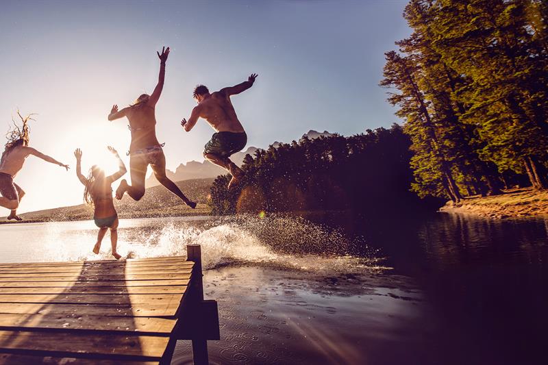 photo of teenagers jumping off of a dock into a lake
